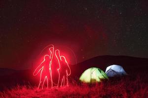 Figures of people by neon lighting. Two iluminated tents under stars at mountains at night photo