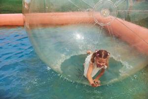 Cheerful little girl have fun inside of floating water walking ball photo