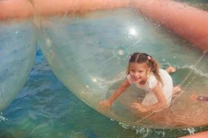 Cheerful little girl have fun inside of floating water walking ball photo
