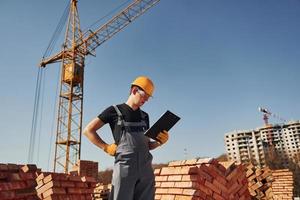 Holds notepad with documents. Construction worker in uniform and safety equipment have job on building photo