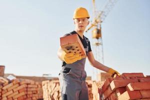 Holds brick in hand. Construction worker in uniform and safety equipment have job on building photo