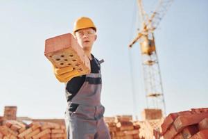 Holds brick in hand. Construction worker in uniform and safety equipment have job on building photo