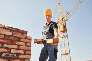 Holds bricks in hands. Construction worker in uniform and safety equipment have job on building photo