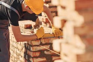 Measures of brick wall. Construction worker in uniform and safety equipment have job on building photo