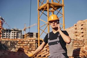 Talking by phone. Construction worker in uniform and safety equipment have job on building photo