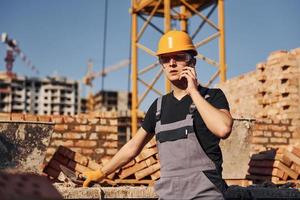 Talking by phone. Construction worker in uniform and safety equipment have job on building photo