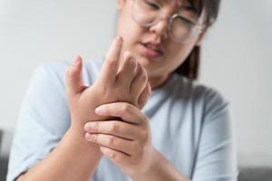 Closeup woman sitting on sofa holds her wrist. hand injury, feeling pain. Health care and medical concept. photo