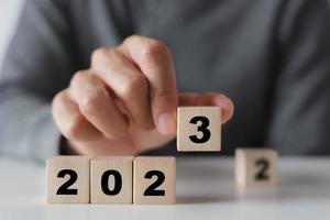 mano de hombre poniendo bloque de cubo de madera para cambiar el año 2022 al año 2023. comienzo del año 2023. concepto de feliz año nuevo. foto