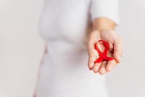 Closeup woman hand holding red ribbon HIV, world AIDS day awareness ribbon. Healthcare and medicine concept. photo