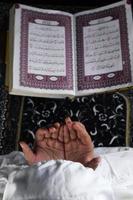 child hand praying with raised hands against the Quran background. Islamic concept photo