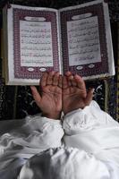 child hand praying with raised hands against the Quran background. Islamic concept photo