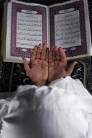 child hand praying with raised hands against the Quran background. Islamic concept photo