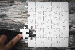 Pieces of jigsaw puzzle in woman's hands. White details of jigsaw puzzle piece on wooden background. Concept of working together as a business team. The idea of getting involved, working for success. photo