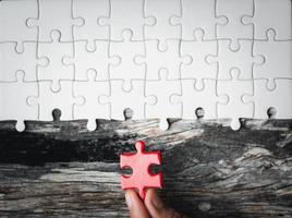 Pieces of jigsaw puzzle in woman's hands. White details of jigsaw puzzle piece on wooden background. Concept of working together as a business team. The idea of getting involved, working for success. photo