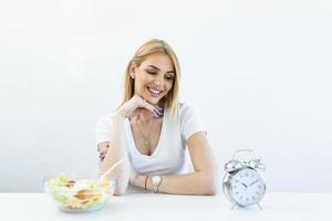 mujer joven sosteniendo reloj y comida saludable de ensalada concepto de ayuno intermitente. tiempo para perder peso, control de la alimentación o tiempo para el concepto de dieta. foto