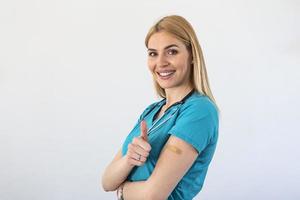 médico joven vacunado, trabajador médico, mujer enfermera gesticulando con el pulgar hacia arriba aprobando la vacunación, fondo blanco foto