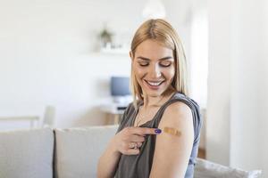 mujer señalando su brazo con un vendaje después de recibir la vacuna covid-19. mujer joven mostrando su hombro después de recibir la vacuna contra el coronavirus foto