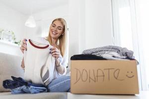 Donation Concept. Woman holding a Donate Box with full of Clothes. Woman holding a book and clothes donate box. Clothes in box for concept donation and reuse recycle photo