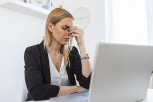 Feeling exhausted. Frustrated young woman looking exhausted while sitting at her working place and carrying her glasses in hand photo