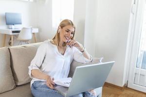 Smiling young woman using laptop at home, looking at screen, chatting, wearing wireless headset having video conference . business trainer tutoring by webcam, online training, e-coaching concept photo