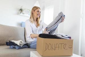 Donation Concept. Woman holding a Donate Box with full of Clothes. Woman holding a book and clothes donate box. Clothes in box for concept donation and reuse recycle photo