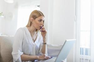 Nervous woman looking at laptop and biting her fingernails at home. Anxious depressed woman sitting with laptop and biting nails, looking nervous worried, scared of deadline stressful job. photo