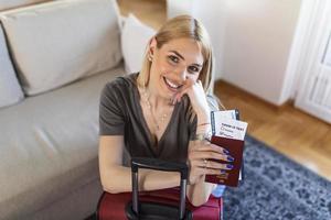 Happy woman planning a travel during covid-19 pandemic, preparing a suitcase. Woman preparing the vacation trip. Holding passport, ticket and negative coronavirus test in hand photo