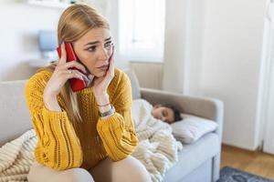 niño enfermo con termómetro acostado en la cama tomando temperatura. niño enfermo con fiebre y enfermedad en la cama. madre hablando por teléfono inteligente con un trabajador de ambulancia foto