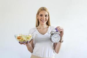 mujer joven sosteniendo reloj y comida saludable de ensalada concepto de ayuno intermitente. tiempo para perder peso, control de la alimentación o tiempo para el concepto de dieta. foto