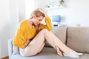 Woman lying on sofa looking sick in the living room. Beautiful young woman lying on bed and holding hands on her stomach. Woman having painful stomachache on bed, Menstrual period photo