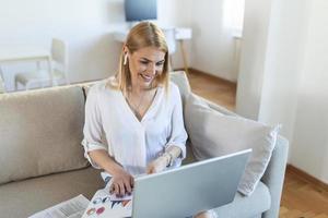 mujer joven sonriente que usa una computadora portátil en casa, mira la pantalla, chatea, usa auriculares inalámbricos y tiene una videoconferencia. tutoría de formadores de negocios por cámara web, formación en línea, concepto de e-coaching foto