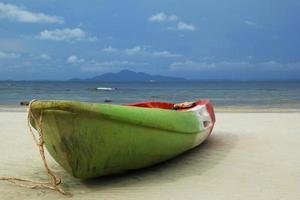 Travel to island Phi Phi, Thailand. The green-red-white boat on the sand beach with sea and a mountain and blue sky on background. photo