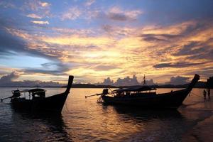 los botes de cola larga cerca de una playa durante una puesta de sol. krabi, tailandia. foto