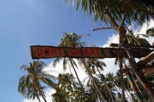 Koh Lanta, Thailand. An inscription - Dont worry - on the wooden abandoned hut on the palms tree and sky background. photo