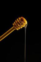 Wooden spoon for honey on black background and liquid fresh honey flowing down it. photo