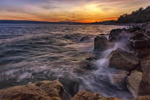 Sunset over the sea with splash waves on the rocks photo