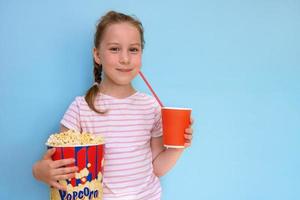 cute girl with a pigtail holding a big glass of popcorn and a glass of cola on a blue background photo