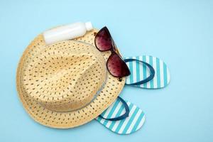 straw hat, sunglasses striped flip flops sun cream on blue background, summer background photo