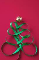 Festive tree made of satin green ribbon on red background. Color of the year 2023 - Viva Magenta photo