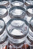 muchas copas de vidrio transparente. producción de cristalería. vasos vacíos con bordes decorativos en fábrica. venta de vajilla en tienda.