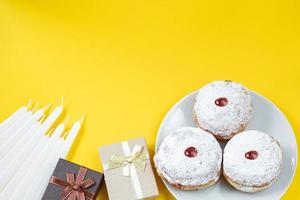 Happy Hanukkah. Jewish dessert Sufganiyot on yellow background. Symbols of religious Judaism holiday. Donuts, candles and gift. photo