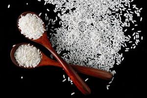 White uncooked rice in wooden spoons on black background. Raw grains of long rice. photo