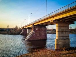 antiguo puente sobre el río con pilares de piedra. flujo rápido de agua en primavera. vista del atardecer foto