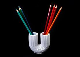 Color pencils for the drawing, located in a support as a vase, focus in front. multi-colored pencils and felt-tip pens in a plaster vase in the shape of a pipe on a black background. photo