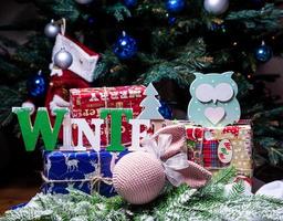 la inscripción invierno de un árbol en año nuevo. en las ramas de abeto contra el fondo de una capa de nieve hay bolas azules y blancas de año nuevo con conos de abeto y una caja con un regalo. Navidad foto