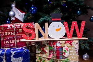 The inscription snow from a tree on a New Year's. On the spruce branches against the background of a snow cover are New Year's blue, white balls with spruce cones and a box with a gift. Christmas photo