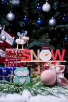 la inscripción nieve de un árbol en año nuevo. en las ramas de abeto contra el fondo de una capa de nieve hay bolas azules y blancas de año nuevo con conos de abeto y una caja con un regalo. Navidad foto