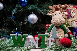 The inscription winter from a tree on a New Year's. On the spruce branches against the background of a snow cover are New Year's blue, white balls with spruce cones and a box with a gift. Christmas photo