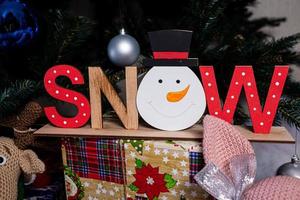 The inscription snow from a tree on a New Year's. On the spruce branches against the background of a snow cover are New Year's blue, white balls with spruce cones and a box with a gift. Christmas photo