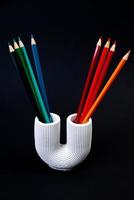 Color pencils for the drawing, located in a support as a vase, focus in front. multi-colored pencils and felt-tip pens in a plaster vase in the shape of a pipe on a black background. photo